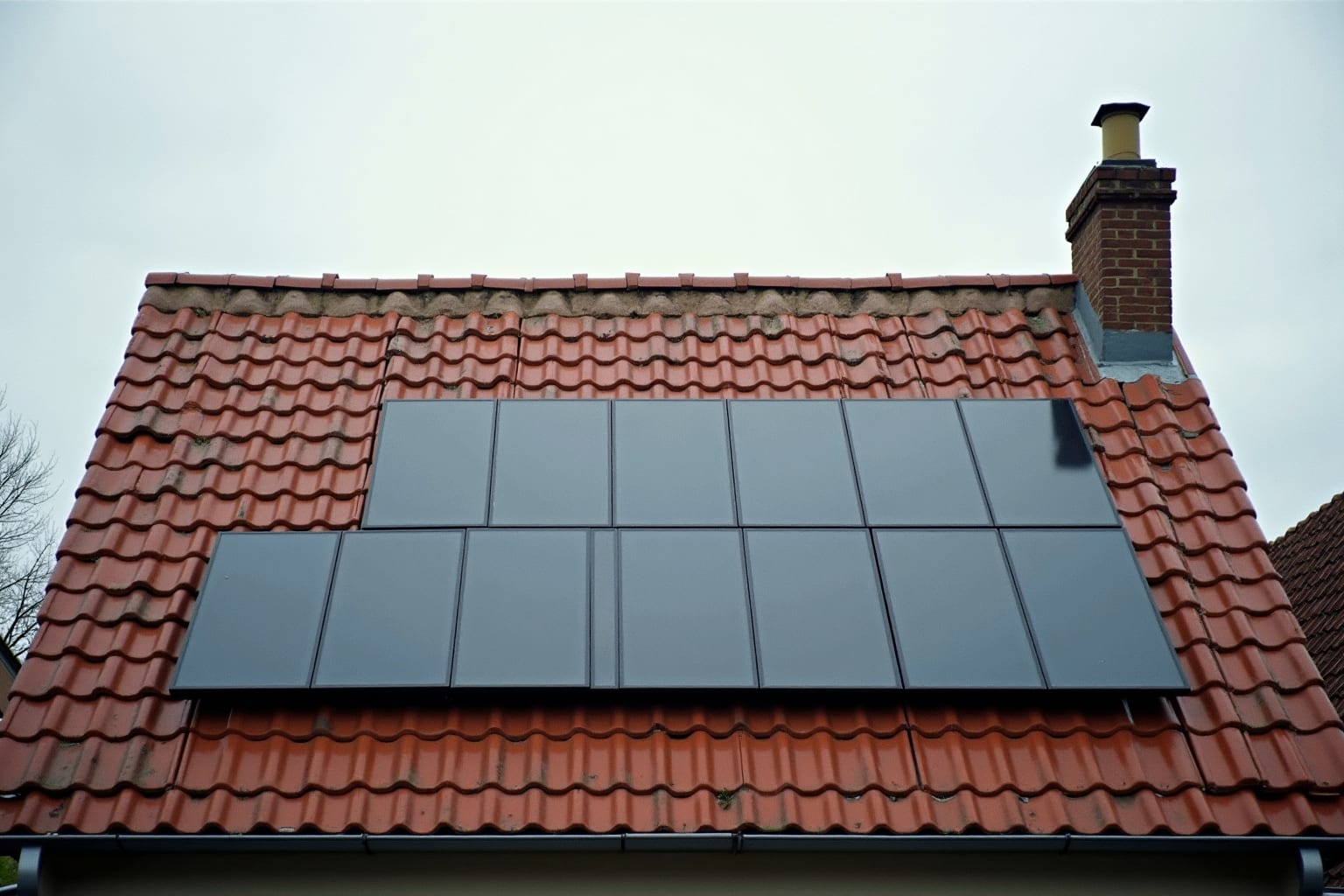 Twee rijen zonnepanelen op een rood pannendak, recht van onderaf gefotografeerd tegen een lichtbewolkte lucht.