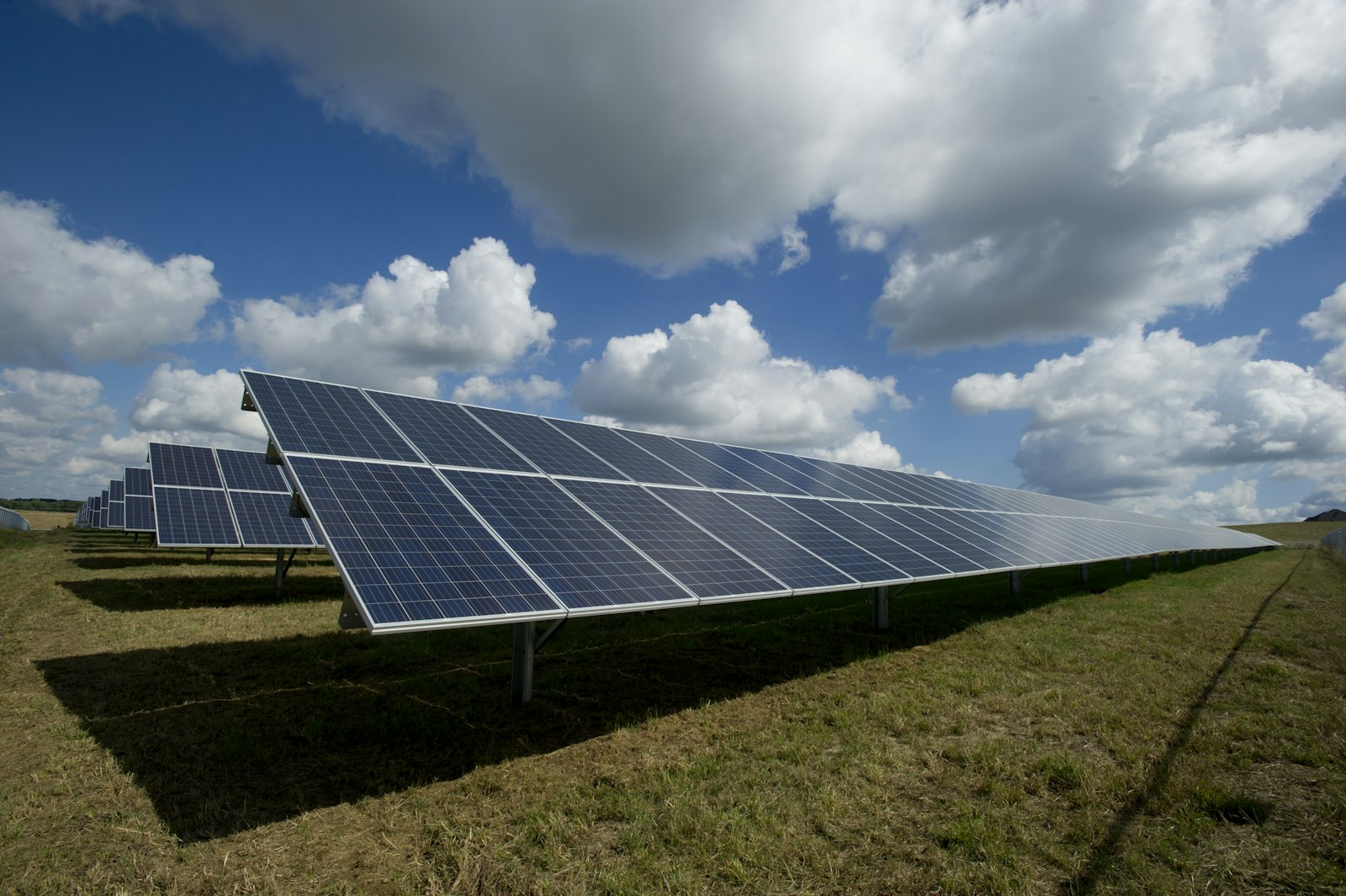 Een uitgestrekt veld met zonnepanelen onder een deels bewolkte hemel.